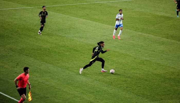 Soccer players on a grassy field, one player in black uniform dribbling the ball.