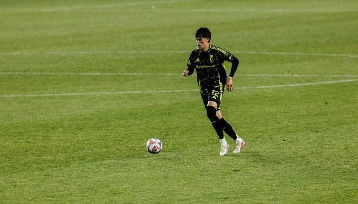 A soccer player in a black and yellow uniform dribbling a ball on a grassy field.