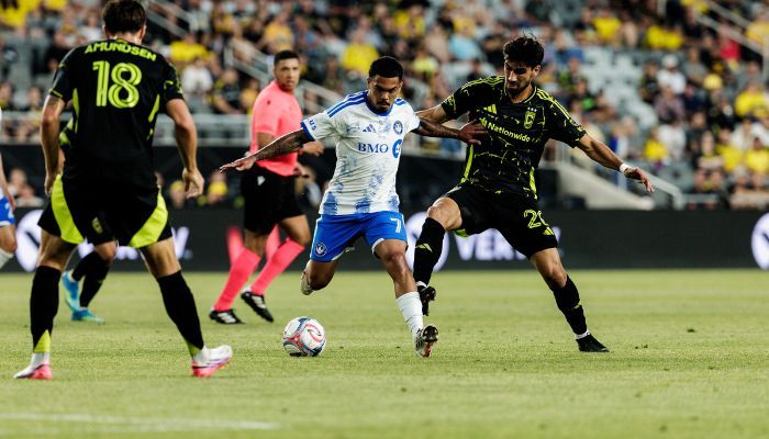 Two soccer players in blue and yellow jerseys competing for the ball on a soccer field.