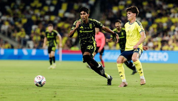 Two soccer players in green and yellow jerseys running on a soccer field, one player dribbling the ball.