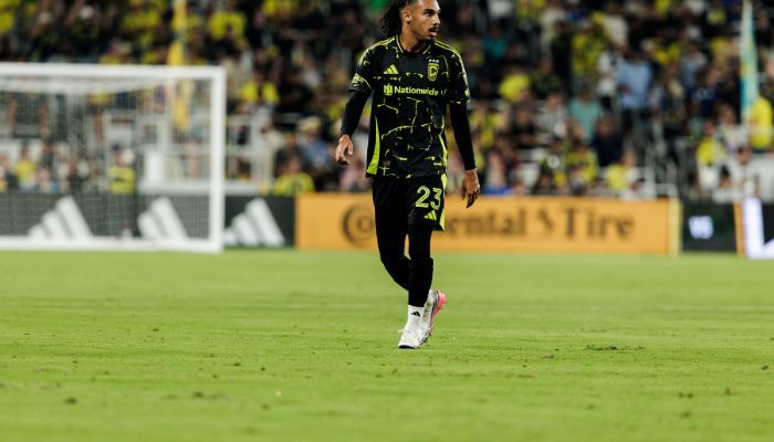 A soccer player wearing a black and neon green jersey with the number 23 running on a soccer field.