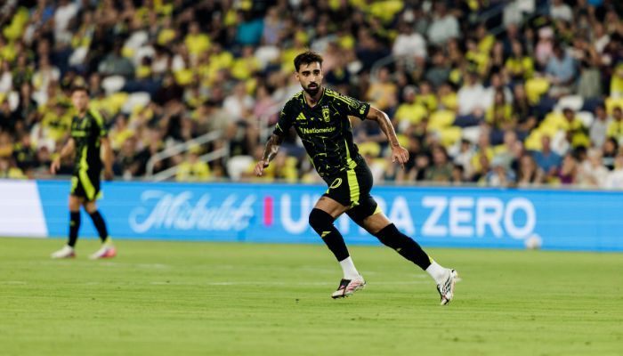 A soccer player in a green jersey running on a field with spectators in the background.