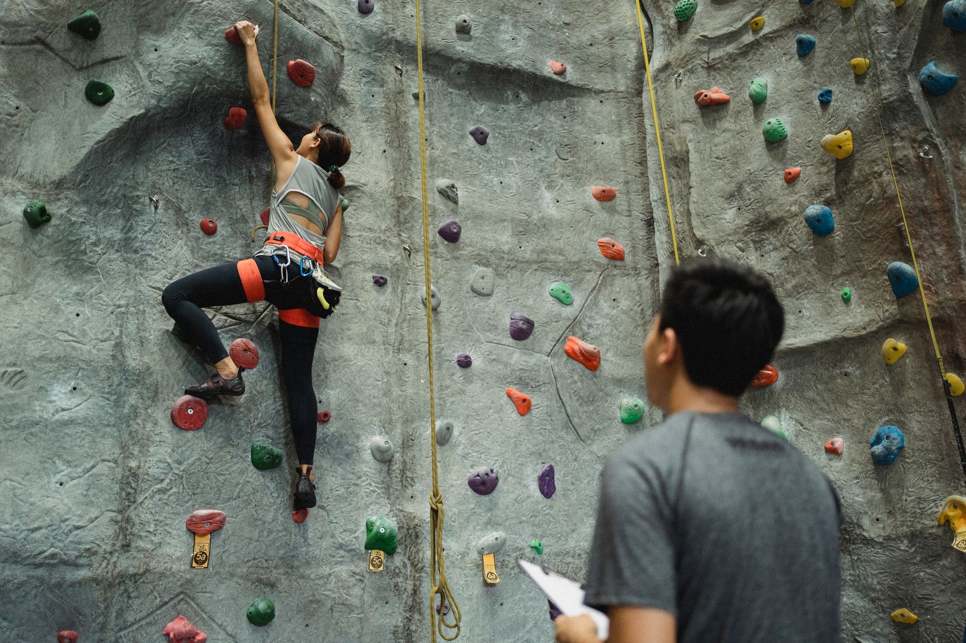 referee watching on slim female climbing on gray wall