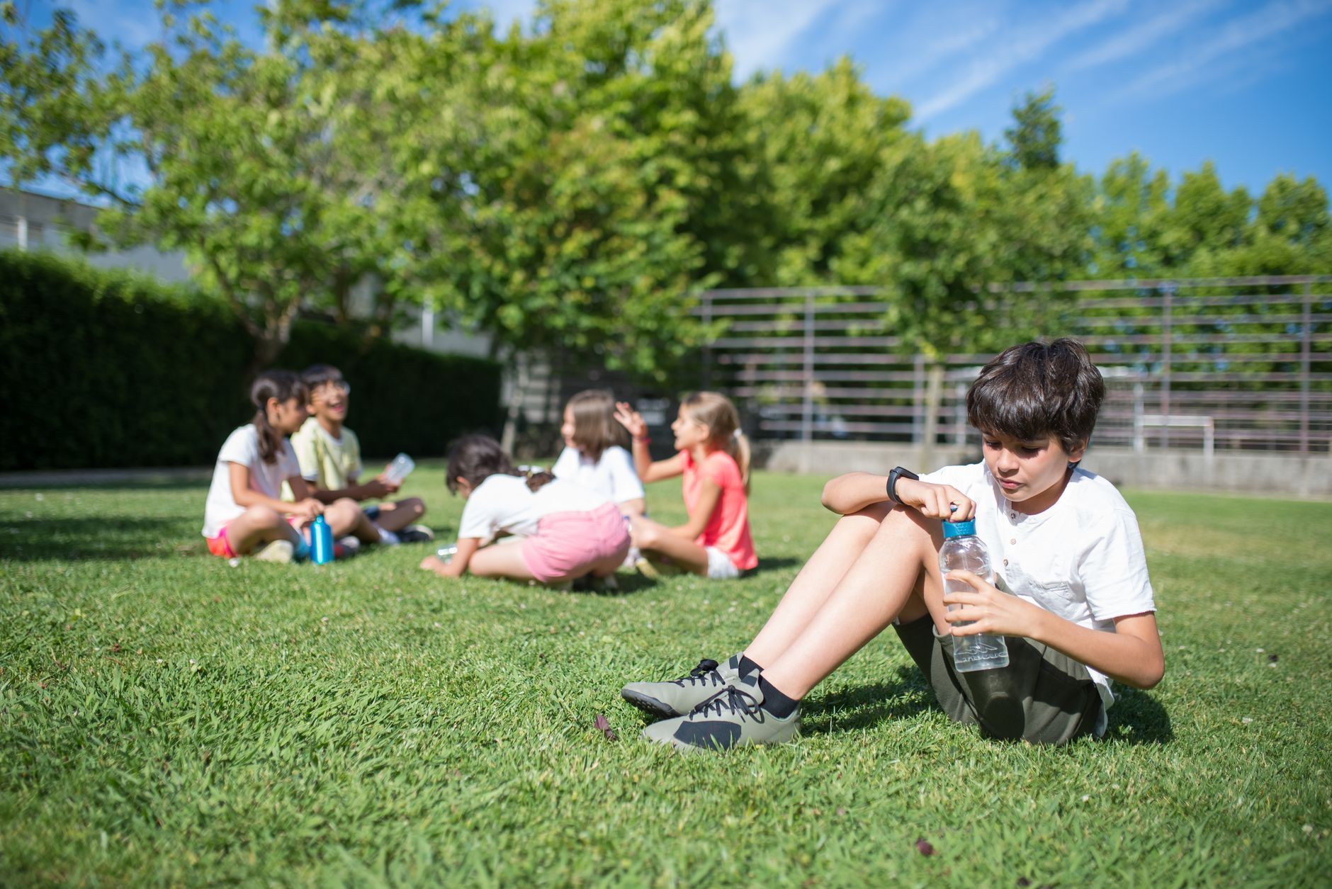 a boy holding a water bottle while sitting on the grass
